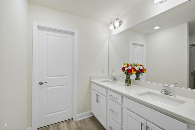 bathroom featuring a sink, baseboards, wood finished floors, and double vanity