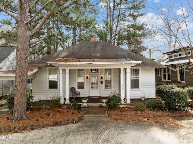 view of front of house with a shingled roof, covered porch, and a chimney