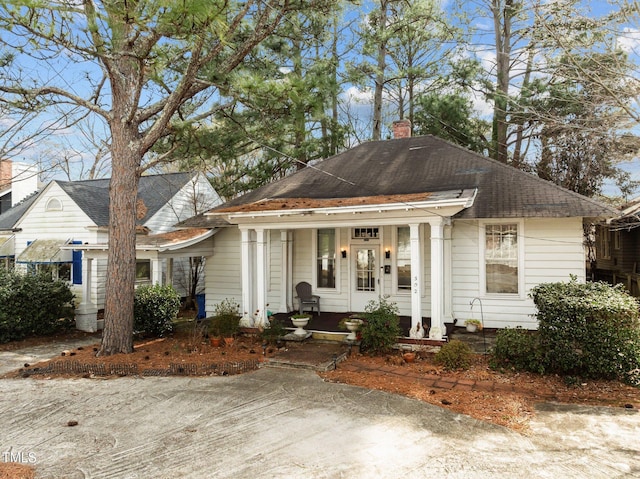 bungalow-style house with a porch, a shingled roof, and a chimney