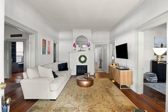 living area featuring a brick fireplace, dark wood-style flooring, and crown molding