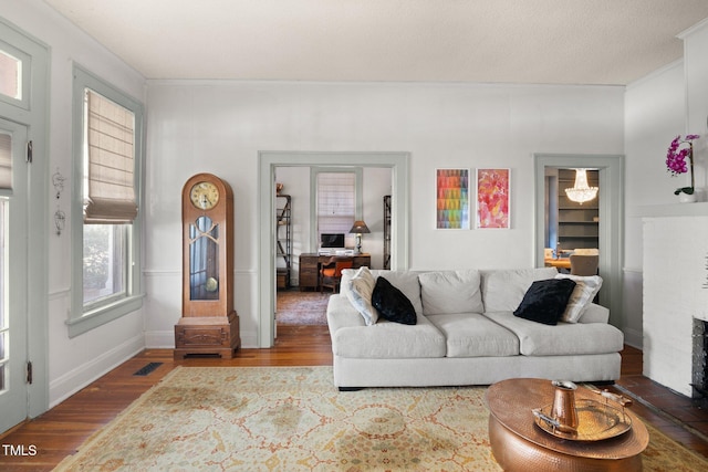 living room featuring baseboards, a brick fireplace, wood finished floors, and crown molding