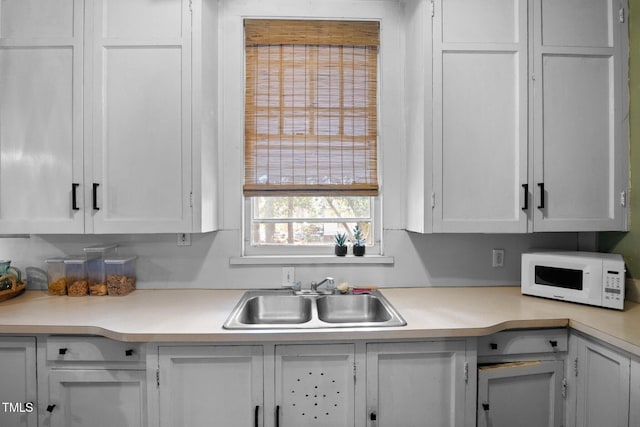 kitchen with white microwave, white cabinetry, light countertops, and a sink