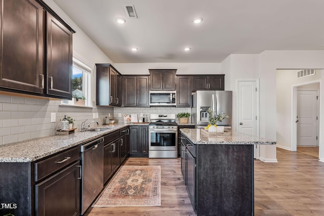 kitchen featuring a center island, visible vents, appliances with stainless steel finishes, dark brown cabinetry, and light wood-type flooring