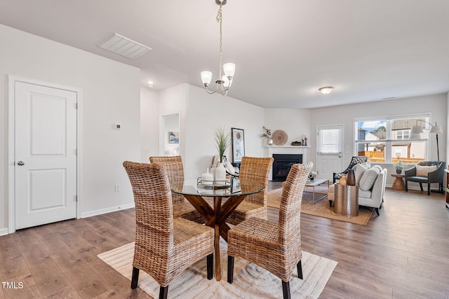 dining room with a chandelier, a fireplace, wood finished floors, visible vents, and baseboards