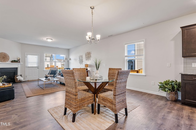 dining space featuring a chandelier, dark wood-type flooring, a fireplace, and baseboards