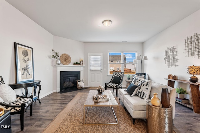 living area featuring a fireplace with flush hearth, baseboards, and wood finished floors