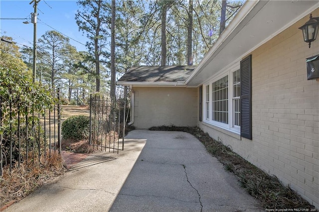 view of side of property with a shingled roof, brick siding, fence, and a patio