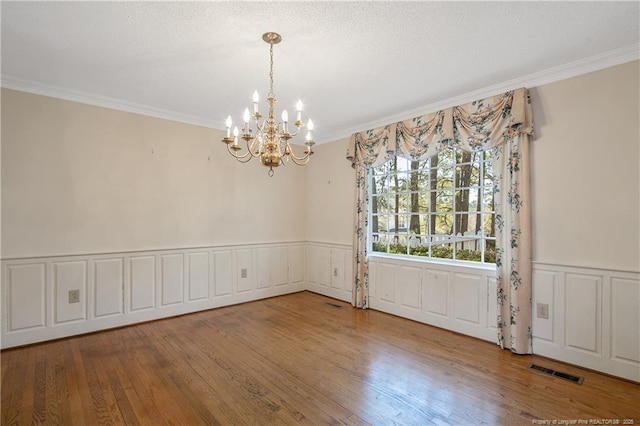 unfurnished dining area with a wainscoted wall, crown molding, a notable chandelier, visible vents, and wood finished floors