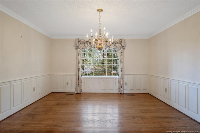 unfurnished dining area with a wainscoted wall, a textured ceiling, and wood finished floors