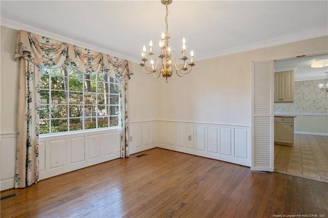 unfurnished dining area featuring an inviting chandelier, visible vents, wood finished floors, and wainscoting