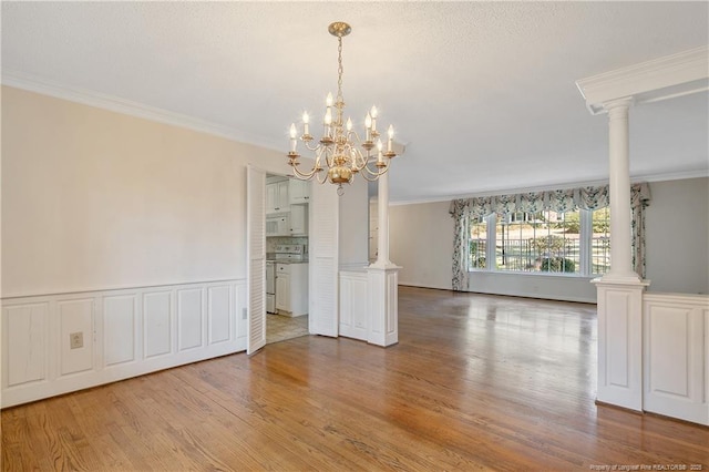 unfurnished dining area with ornate columns, ornamental molding, wood finished floors, and wainscoting