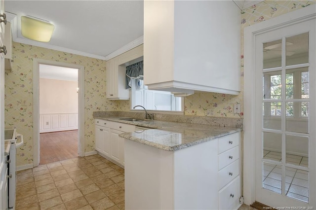 kitchen featuring crown molding, a sink, light stone counters, and wallpapered walls