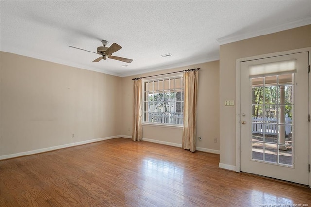 spare room featuring a wealth of natural light, crown molding, visible vents, and wood finished floors