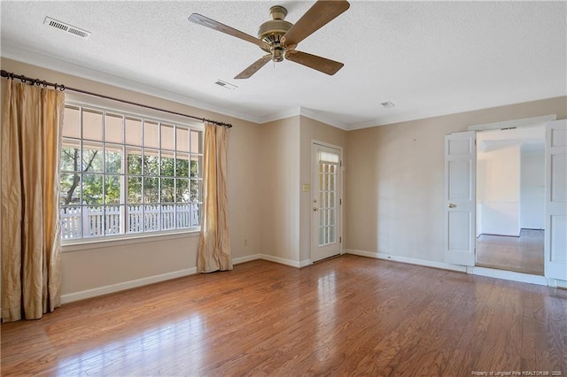 empty room with a textured ceiling, wood finished floors, visible vents, and baseboards