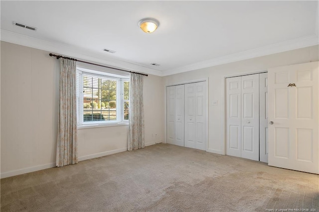 unfurnished bedroom featuring baseboards, visible vents, ornamental molding, carpet flooring, and two closets