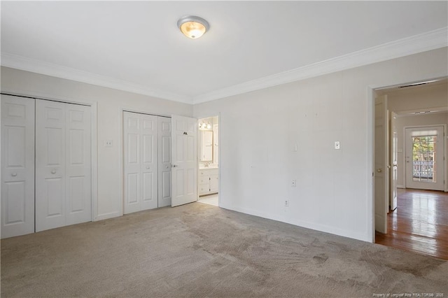 unfurnished bedroom featuring baseboards, connected bathroom, crown molding, carpet flooring, and two closets