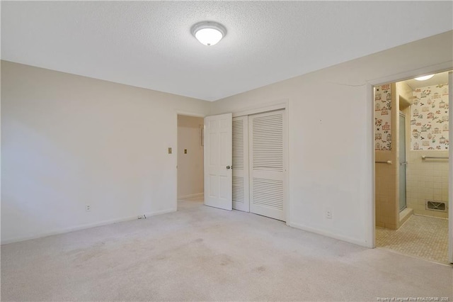 unfurnished bedroom with carpet floors, ensuite bath, a textured ceiling, and a closet