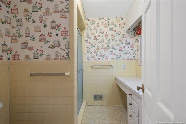 full bath featuring a stall shower, wainscoting, vanity, and wallpapered walls