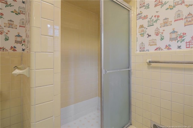 full bath with wallpapered walls, a shower stall, tile walls, and a wainscoted wall