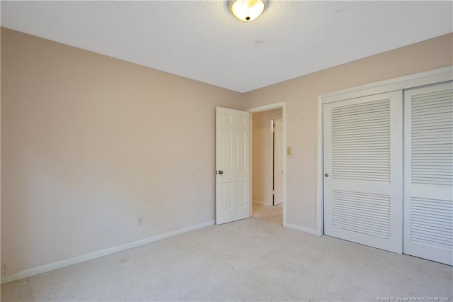 unfurnished bedroom featuring light carpet, a closet, a textured ceiling, and baseboards