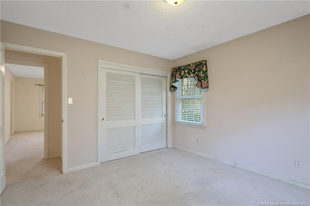 unfurnished bedroom featuring a closet, light colored carpet, a textured ceiling, and baseboards