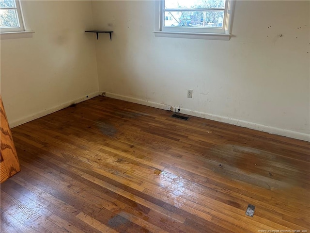 empty room featuring wood-type flooring, plenty of natural light, and baseboards