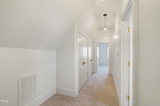 hallway with light colored carpet, visible vents, vaulted ceiling, and baseboards