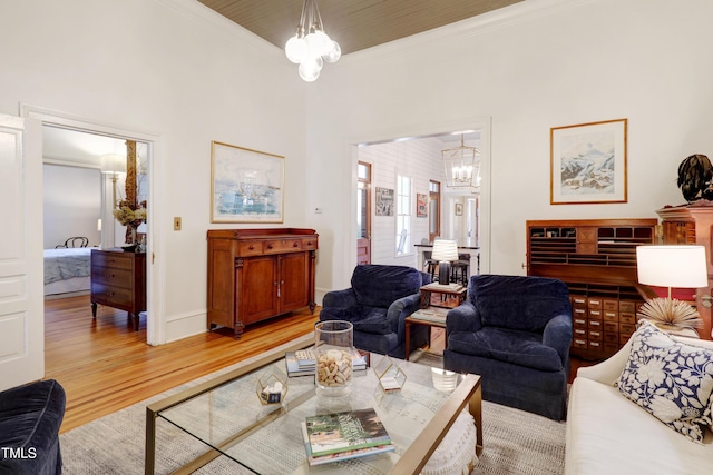 living area with light wood-type flooring, baseboards, ornamental molding, and a notable chandelier