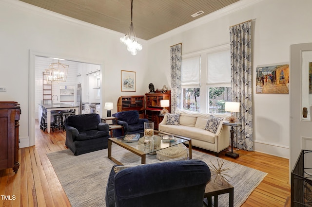 living area featuring crown molding, hardwood / wood-style floors, visible vents, and an inviting chandelier