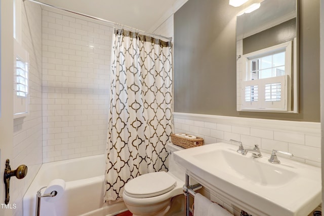 bathroom with toilet, a wainscoted wall, a sink, shower / bath combination with curtain, and tile walls