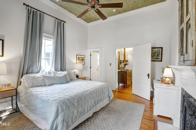 bedroom with wood ceiling, ceiling fan, a fireplace with flush hearth, ornamental molding, and light wood-style flooring