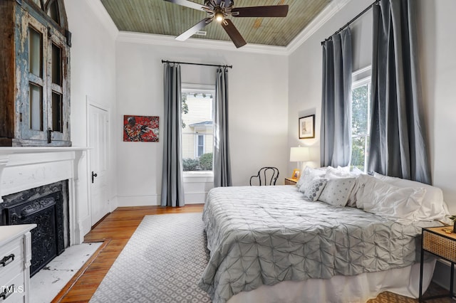 bedroom featuring a ceiling fan, a fireplace, ornamental molding, and wood finished floors