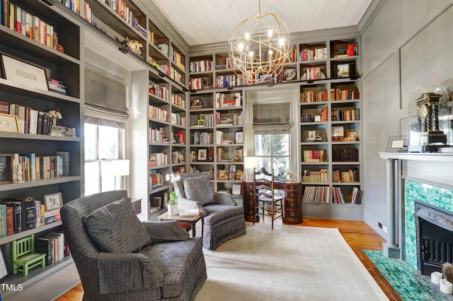 sitting room with a fireplace, wood finished floors, built in features, wall of books, and an inviting chandelier