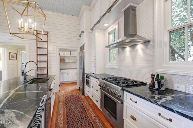 kitchen with light wood-style floors, white cabinetry, a sink, high quality appliances, and wall chimney exhaust hood