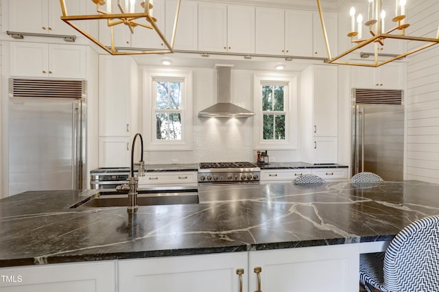 kitchen with a sink, wall chimney range hood, a chandelier, and premium appliances