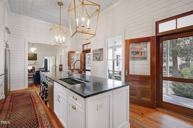 kitchen featuring a sink, light wood-style floors, a wealth of natural light, dark countertops, and a center island with sink