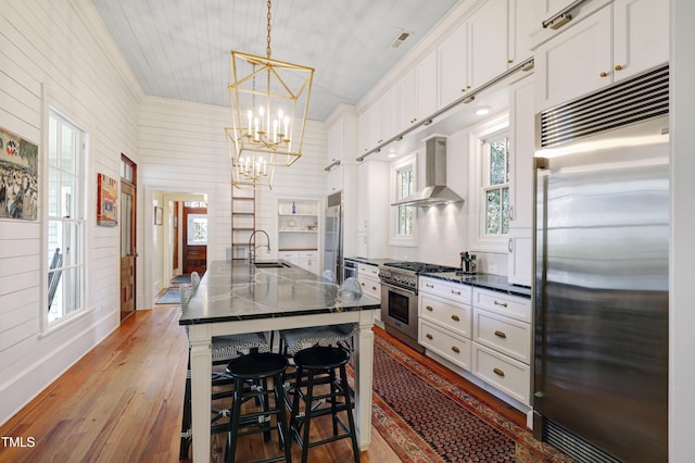 kitchen featuring wall chimney range hood, high quality appliances, white cabinetry, and a sink