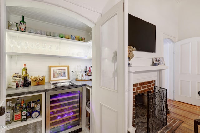 bar with a bar, beverage cooler, a fireplace, and wood finished floors