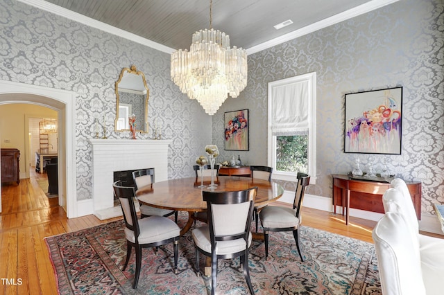 dining space featuring wallpapered walls, arched walkways, wood-type flooring, crown molding, and a notable chandelier