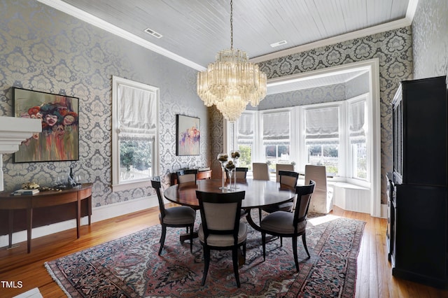 dining area with a chandelier, wood finished floors, crown molding, and wallpapered walls