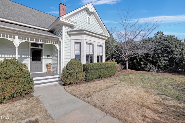 view of front facade featuring a front lawn, a chimney, and a shingled roof