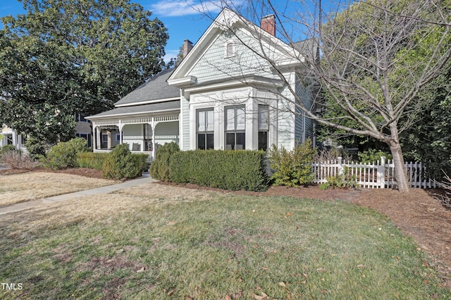 view of front of house with a porch, a chimney, a front yard, and fence