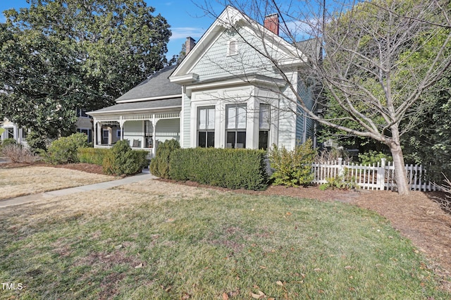 view of front of property with covered porch, fence, a chimney, and a front lawn