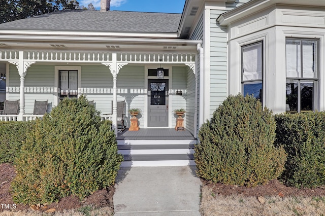 view of exterior entry featuring covered porch and a shingled roof