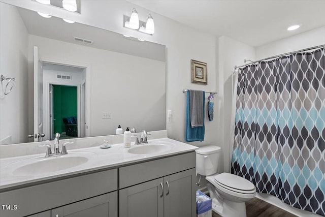 full bathroom with toilet, double vanity, a sink, and visible vents