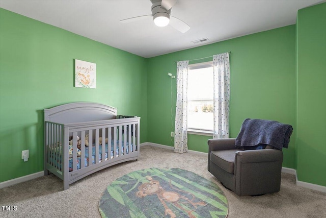 bedroom with a crib, baseboards, visible vents, a ceiling fan, and carpet floors