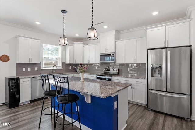 kitchen with stainless steel appliances, visible vents, white cabinets, ornamental molding, and a center island