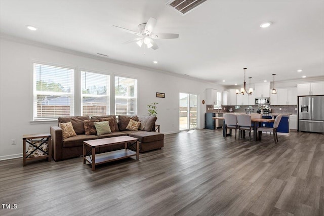 living room featuring dark wood-style flooring, visible vents, and crown molding