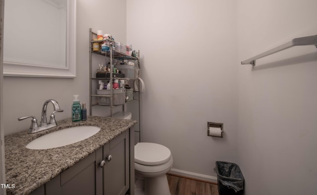 bathroom featuring toilet, baseboards, wood finished floors, and vanity