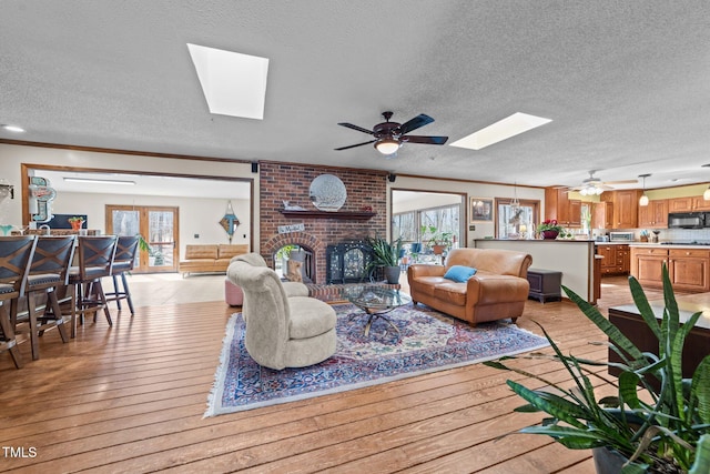 living room with ornamental molding, light wood finished floors, a skylight, and a brick fireplace